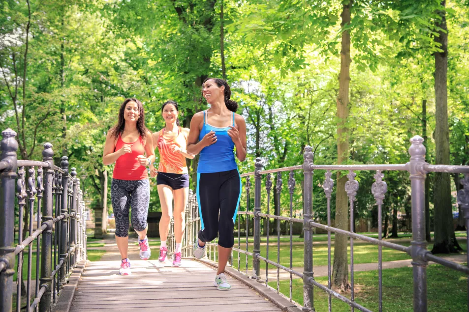 A group of three women running by a river in a park 