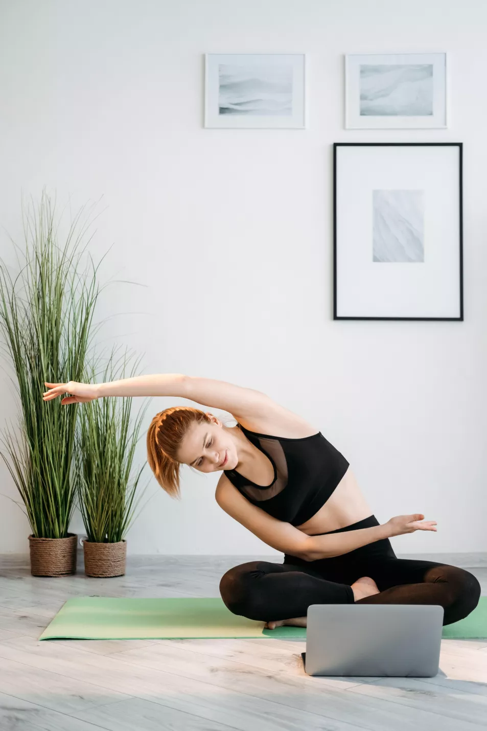 A woman follows a yoga routine at home with her laptop 