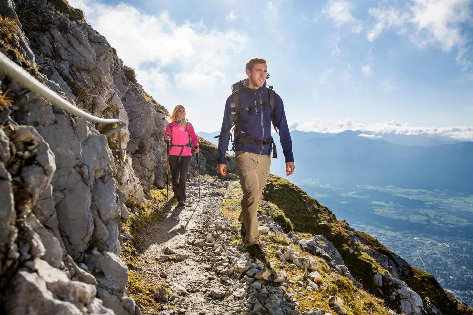 A young man and a young woman climb a mountain pass with a safety rope