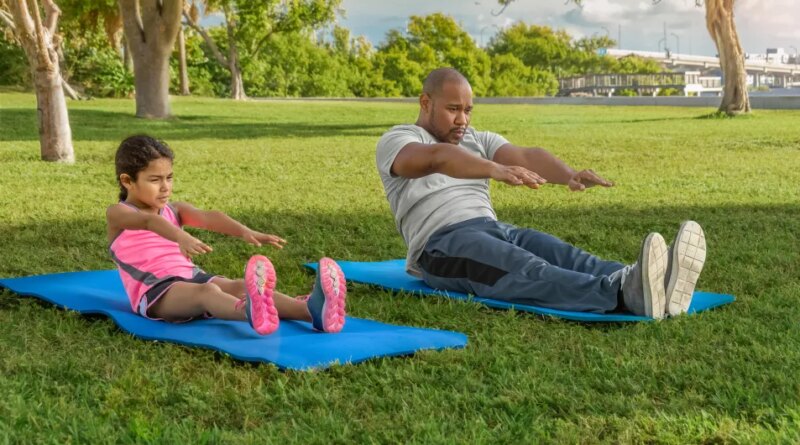 Father and daughter on yoga mats side by side in the park doing sit ups