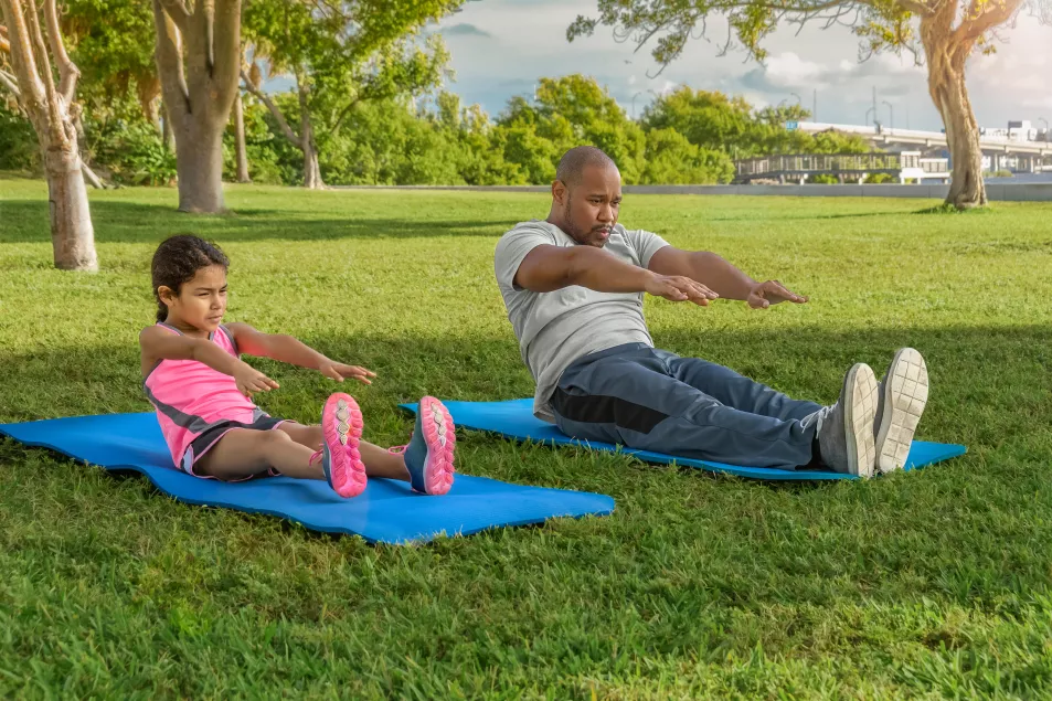 Father and daughter on yoga mats side by side in the park doing sit ups